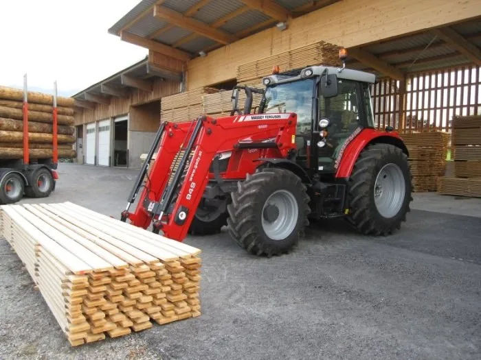 Roter Forsttraktor mit Holzanhänger auf dem Betriebsgelände